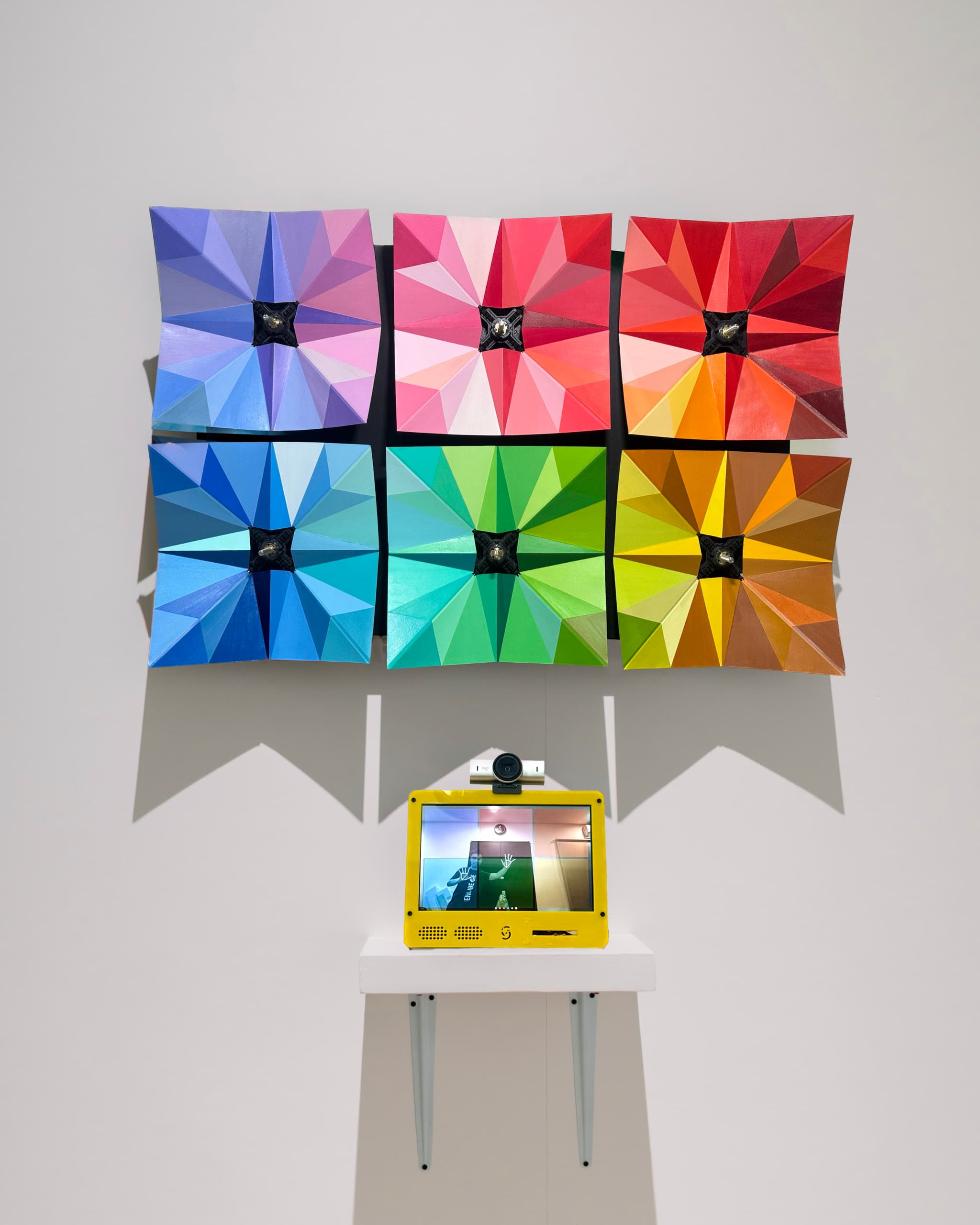 Peccata Pulchra, open: six hand-painted origami panels spread flat in purple, pink, red, blue, green and gold, with a camera kiosk on a shelf below.